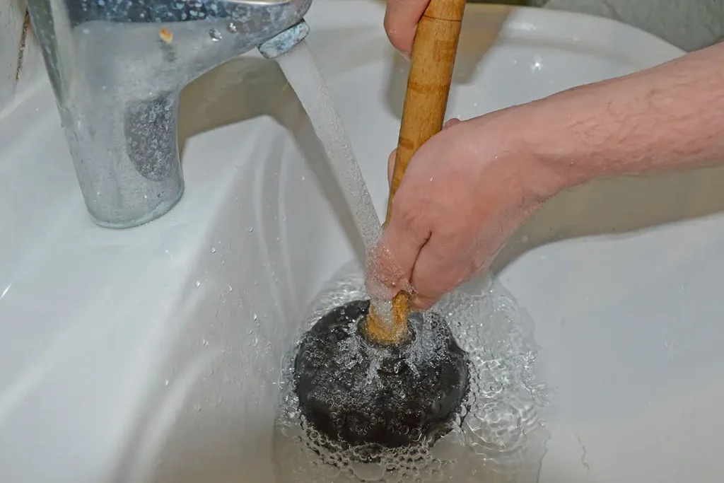 Personne débouchant un lavabo à l’aide d’une ventouse manuelle sous l’eau courante