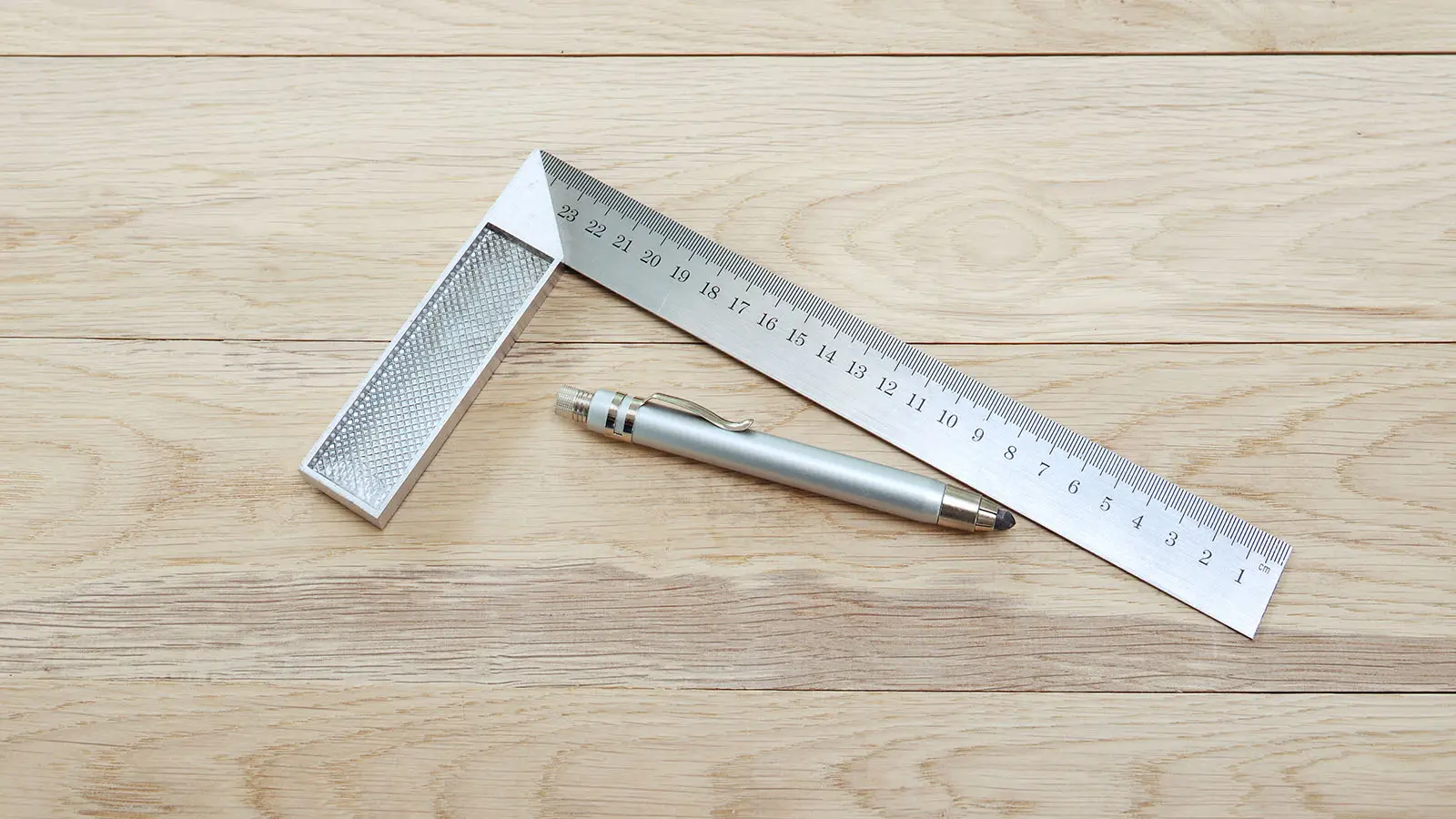 Équerre de mesure en métal et crayon sur un plan de travail en bois clair pour un projet de bricolage maison