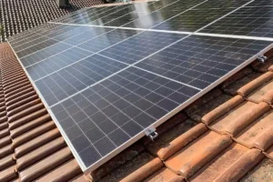 Vue rapprochée de 8 panneaux solaires monocristallins noirs (3 kWc) installés sur une toiture en tuiles rouges à l'aide de rails et fixations en aluminium apparentes, illustrant une installation photovoltaïque pour absorber les pics de consommation diurnes.