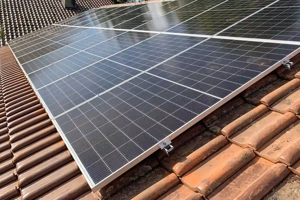 Vue rapprochée de 8 panneaux solaires monocristallins noirs (3 kWc) installés sur une toiture en tuiles rouges à l'aide de rails et fixations en aluminium apparentes, illustrant une installation photovoltaïque pour absorber les pics de consommation diurnes.