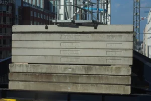 Dalles en béton empilées sur un chantier de construction, avec une grue et un ouvrier à proximité